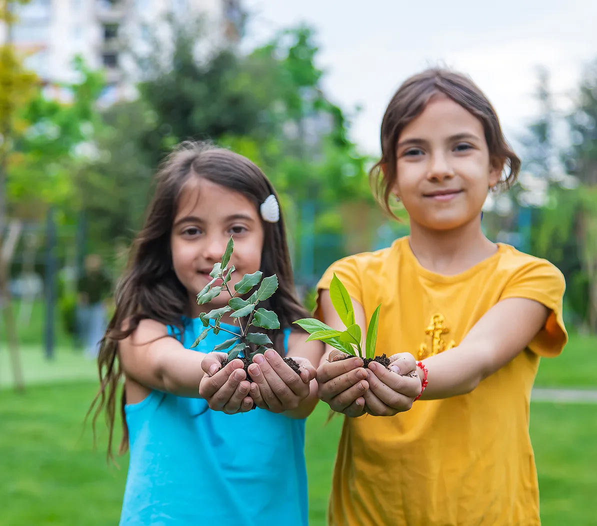 Two children outdoors holding small seedlings in their hands